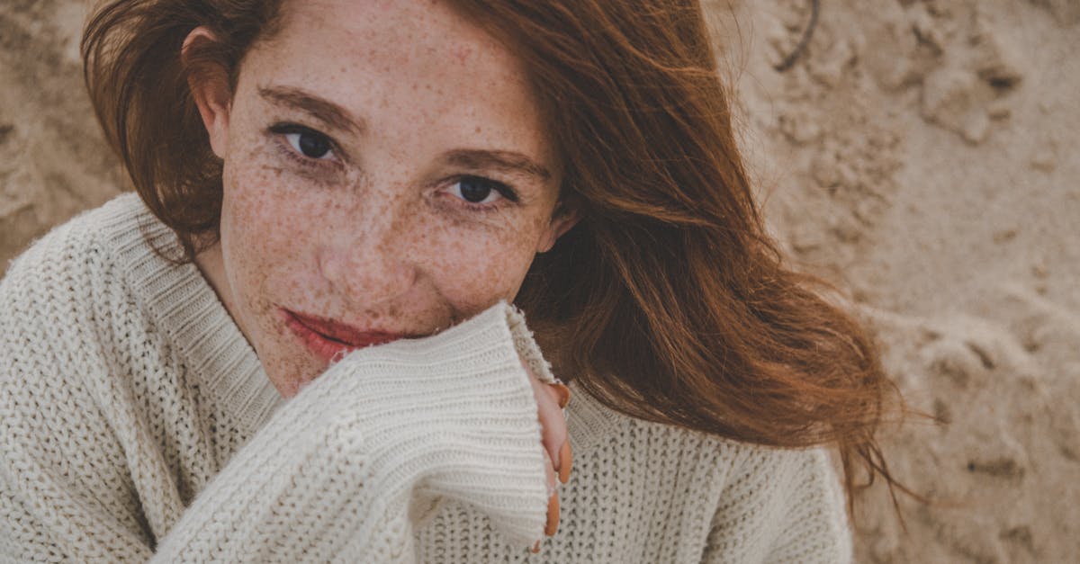 A close-up portrait of a freckled woman with red hair wearing a cozy knitted sweater, exuding warmth and natural beauty.
