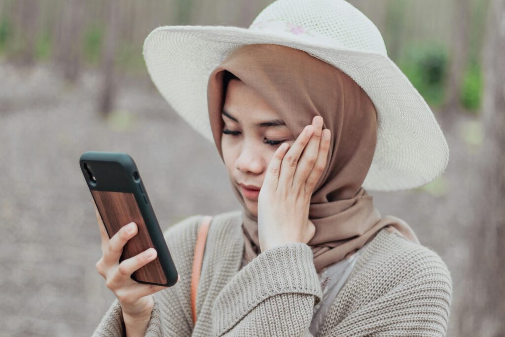 A young woman in a headscarf outdoors looking at her smartphone with a serene expression.