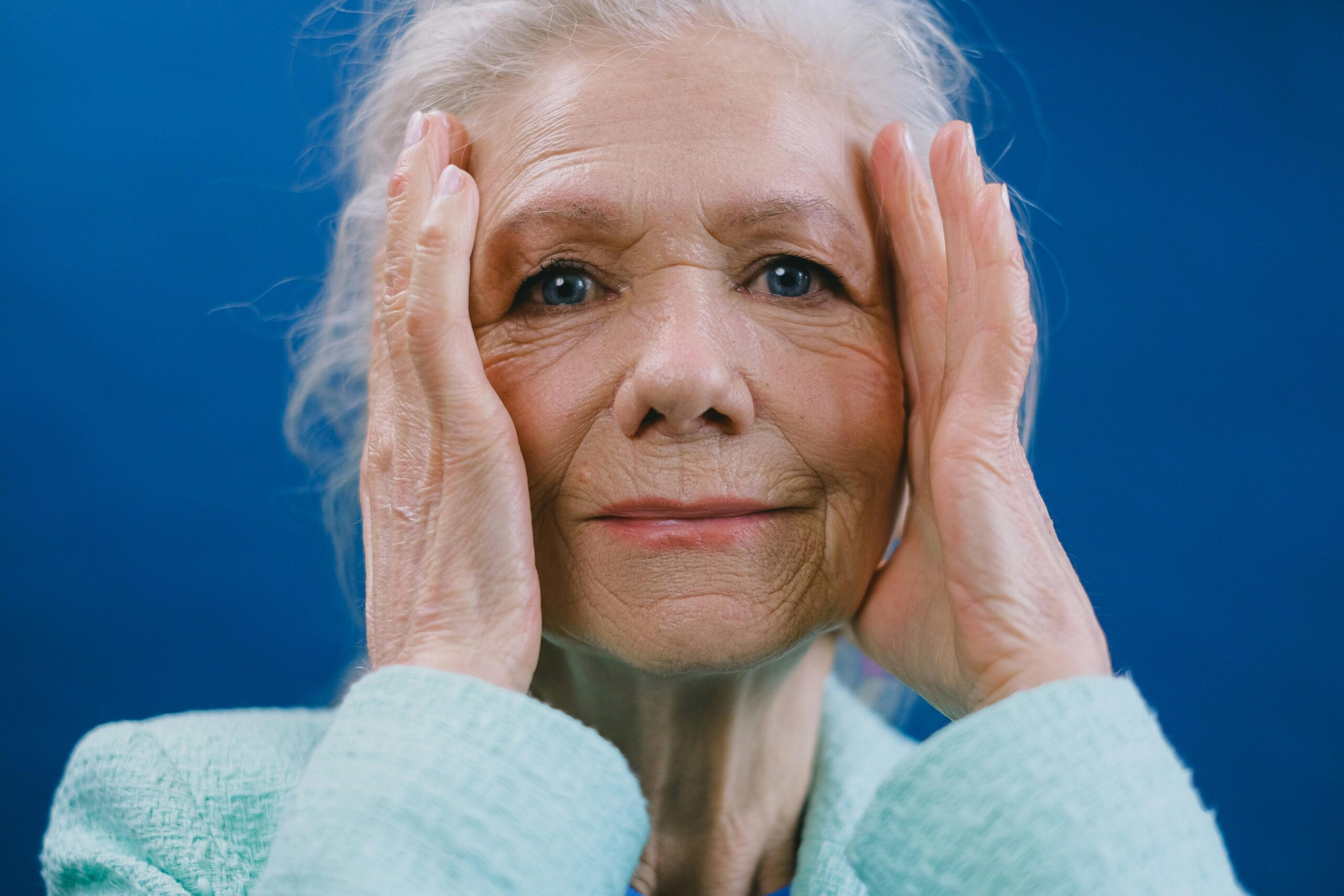 Close-up portrait of an elderly woman holding her face, conveying emotion.