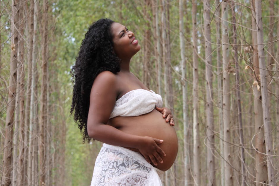 African American pregnant woman with curly hair standing in a serene forest setting.