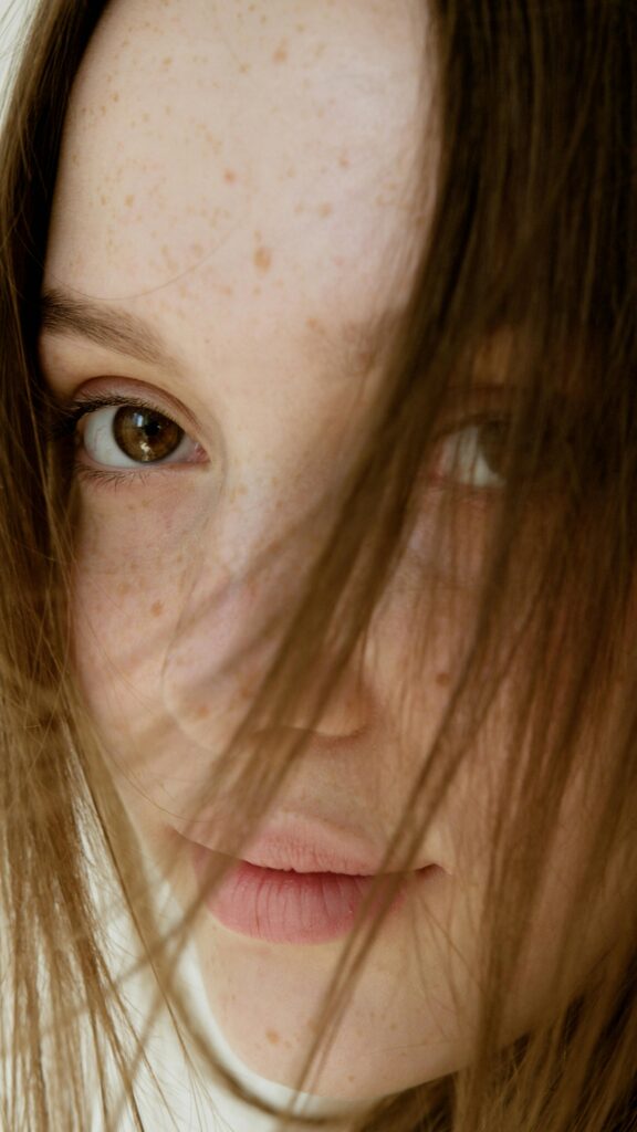 Intimate close-up portrait of a young woman with freckles and flowing hair.